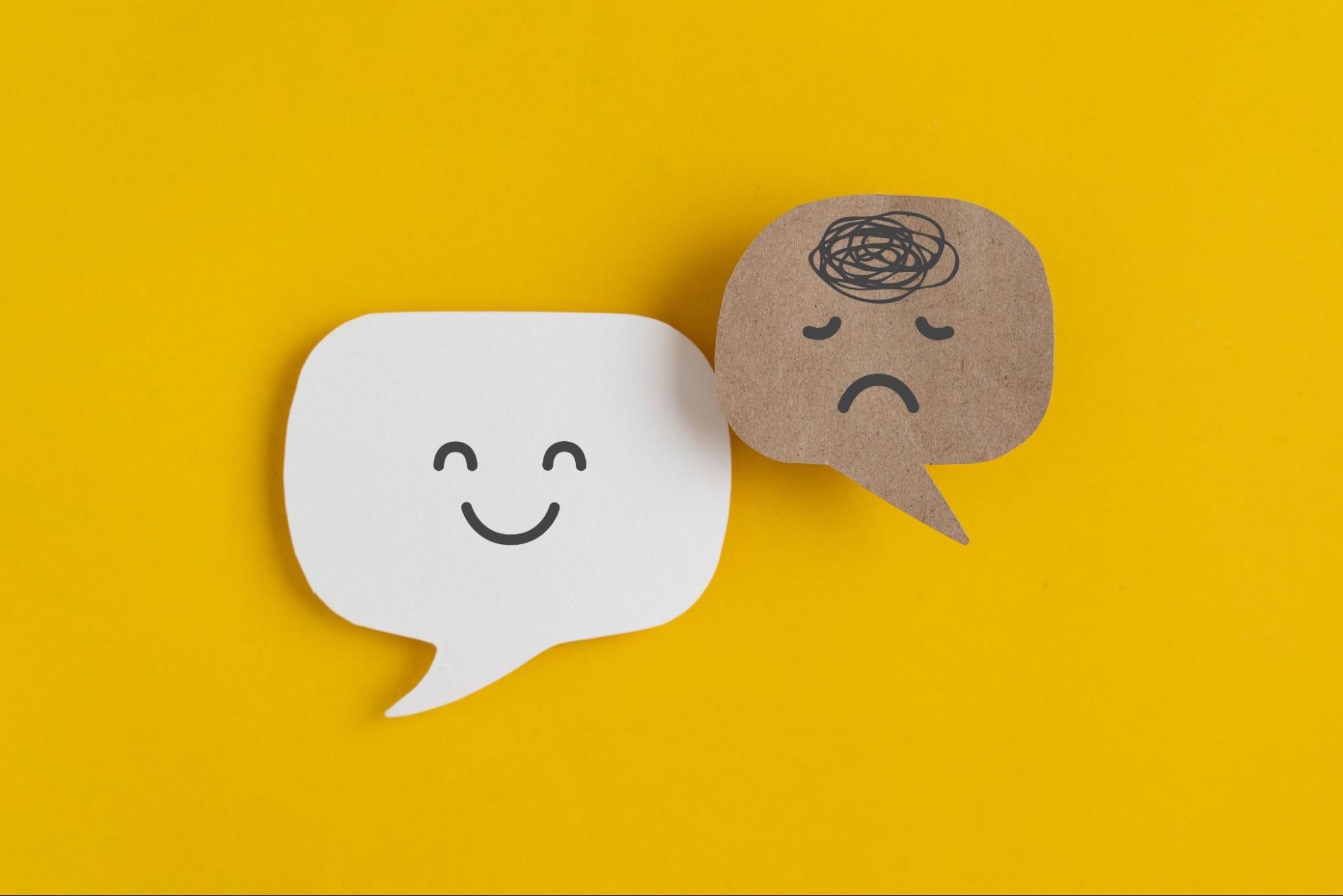 two speech bubbles one with a happy face and one with a sad face to symbolize mental health