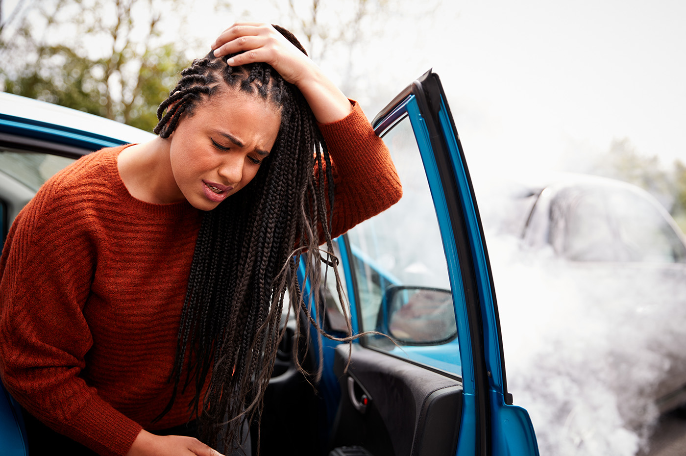 A person standing next to a smoking vehicle holding their head.