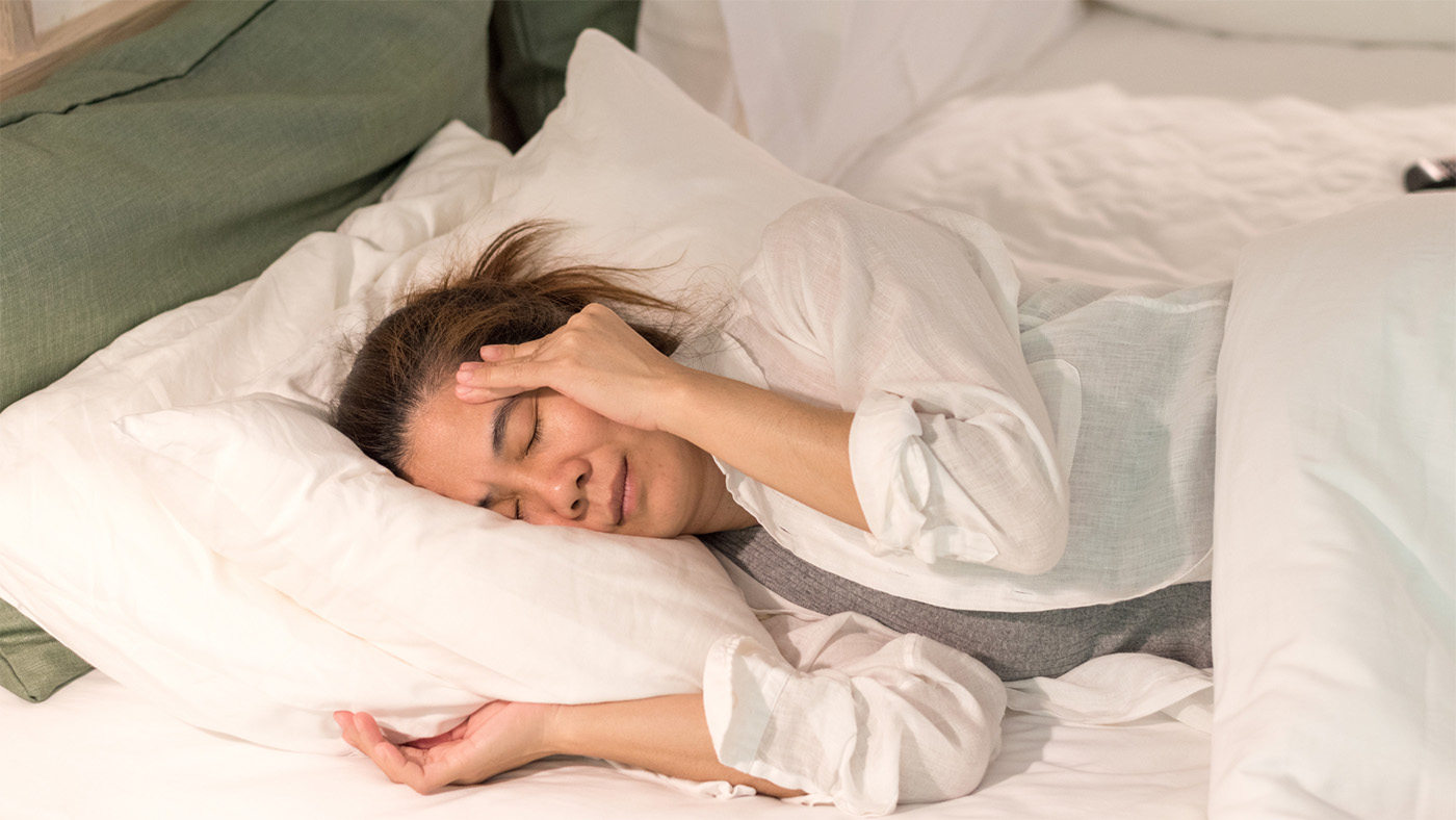 A woman in bed holding her head.