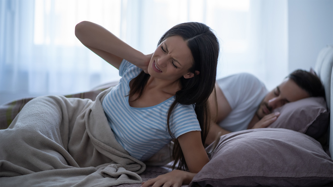 A woman in bed holding her sore neck.