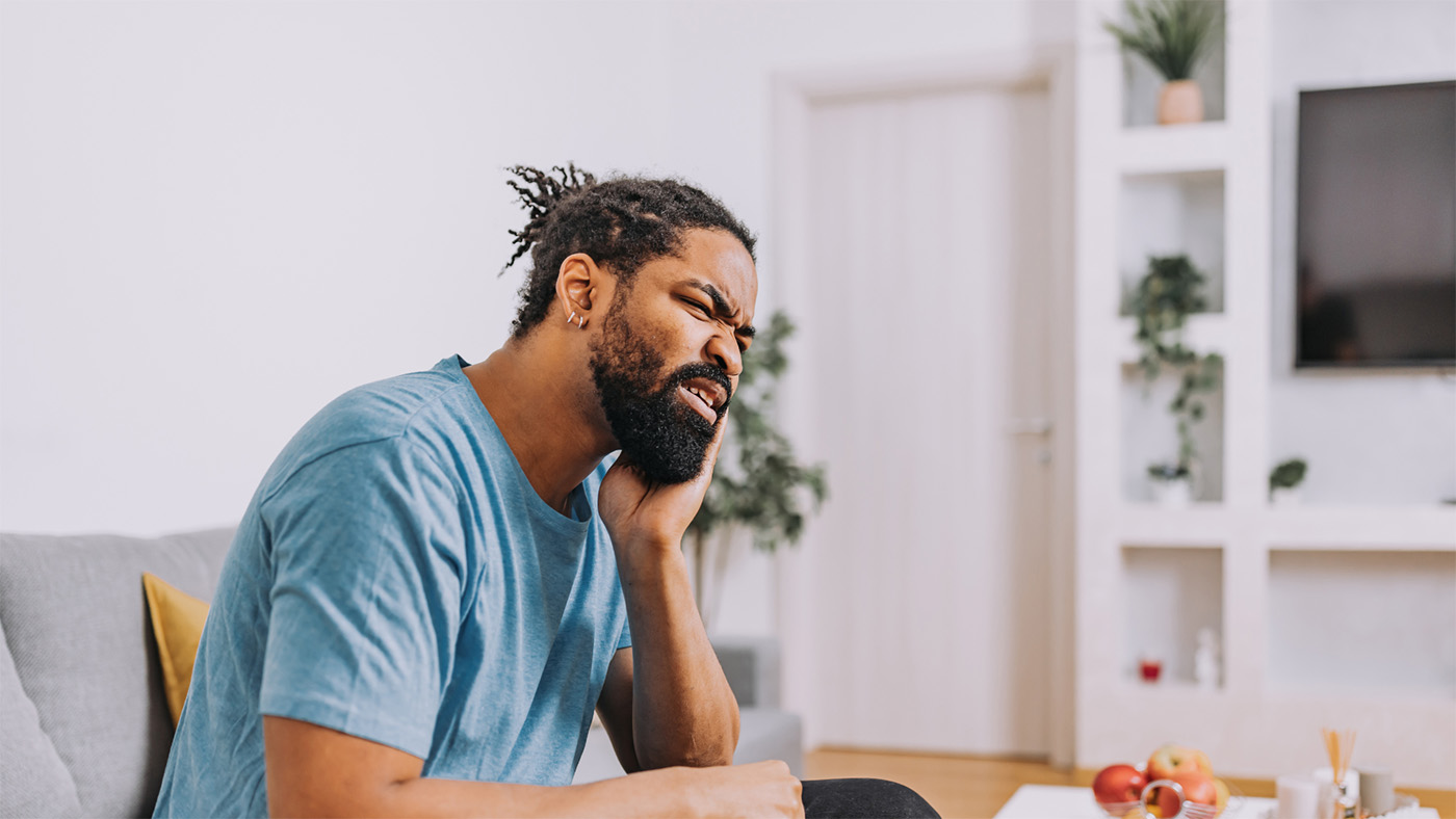 A man sitting at his desk holding his jaw in pain.