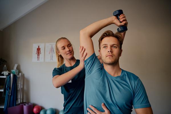 A man working with his Physiotherapist to build arm strength with weights.