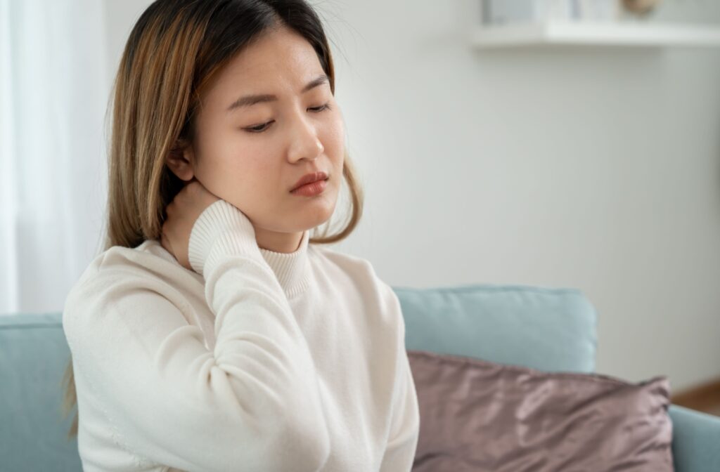 Person sitting on couch holding their neck in discomfort indicating possible chronic neck pain