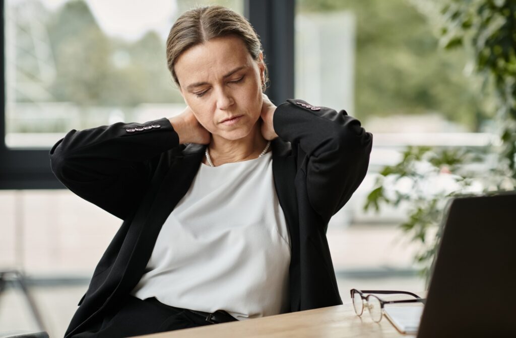 Person sitting at a desk holding their neck in pain.