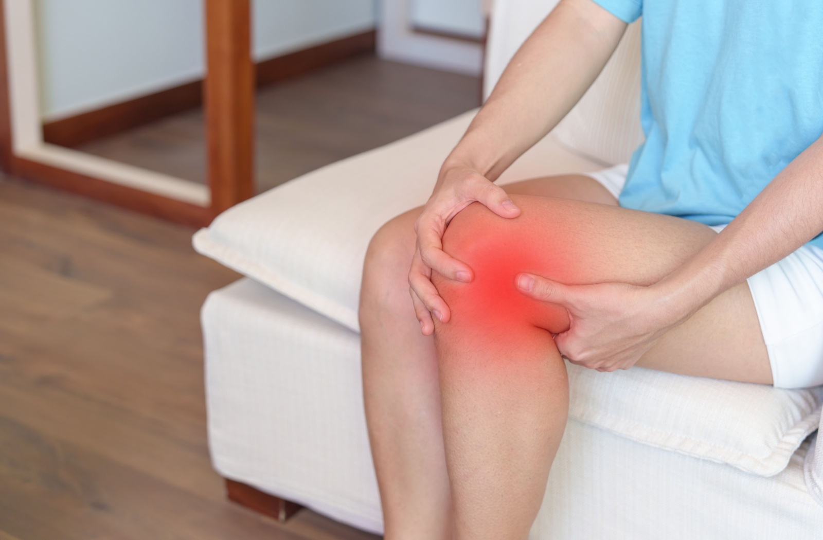 A person sitting on a couch holding their knee in pain.