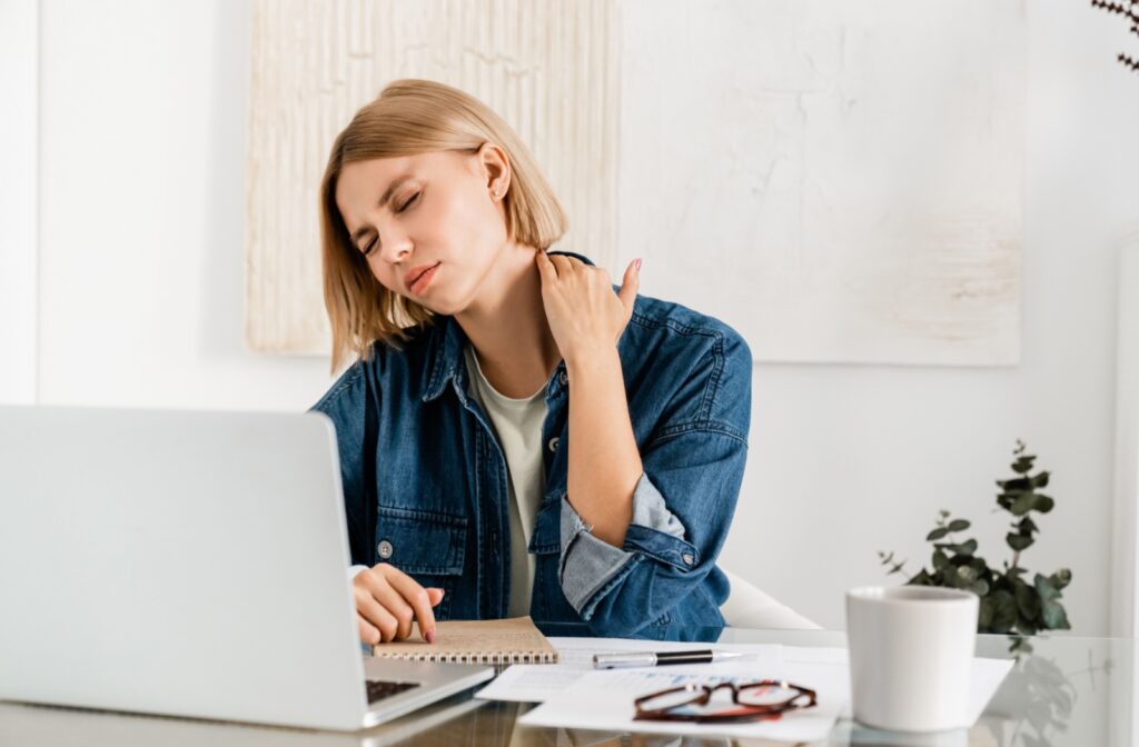 A person sitting at a desk, rubbing their next due to chronic pain.