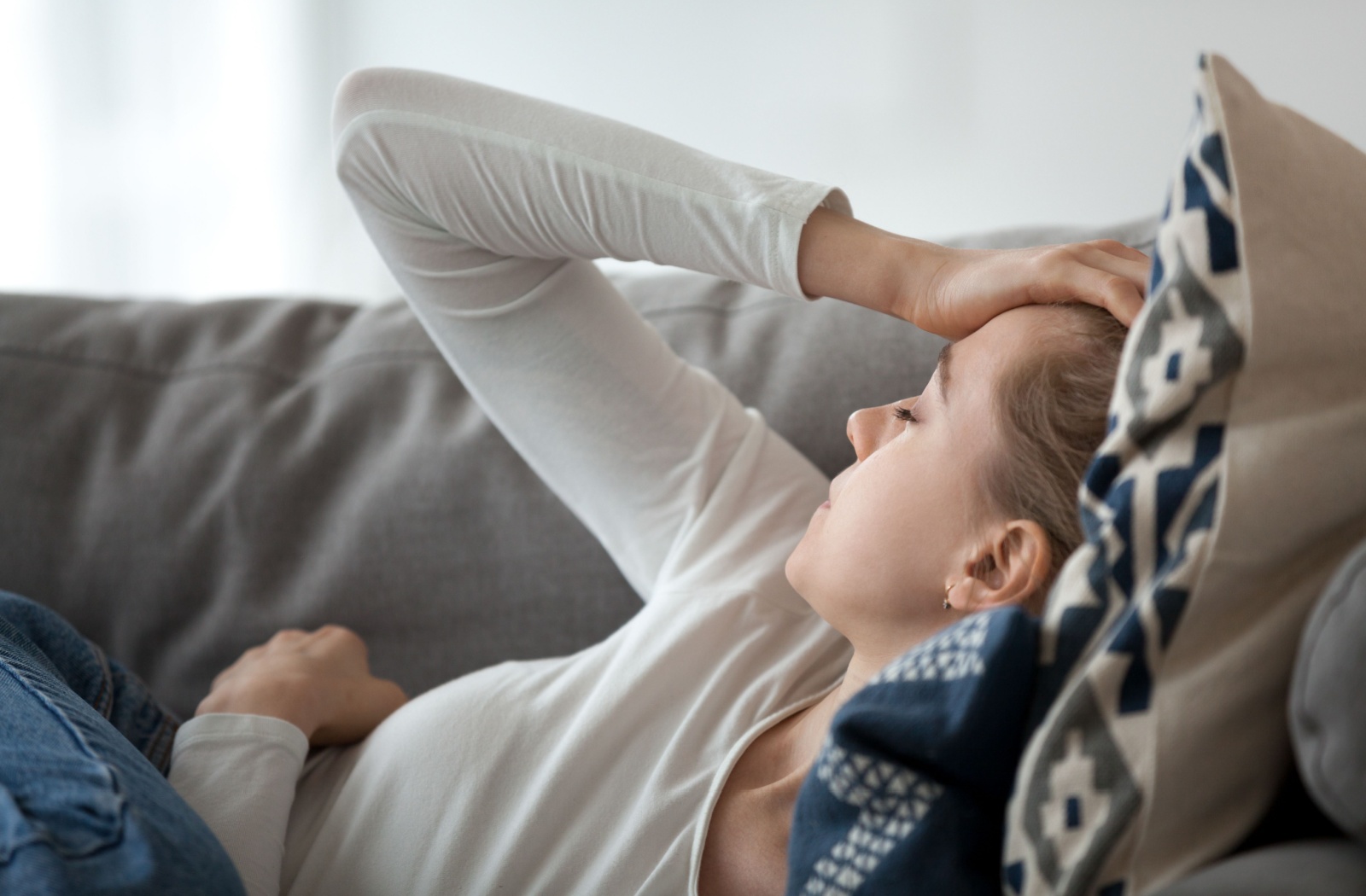 A person laying on a couch with their hand on their head, experiencing the challenges of chronic pain effecting mental health