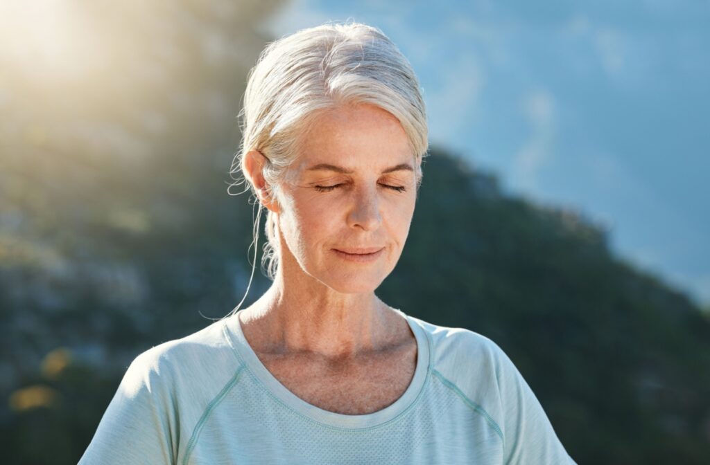A person outside with their eyes closed, practicing deep breathing and calming techniques to help manage chronic pain and mental health.