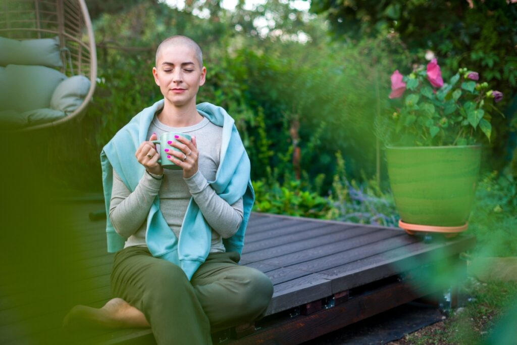 A cancer patient sitting on garden patio with coffee, eyes closed, practicing mindfulness and relaxation techniques.