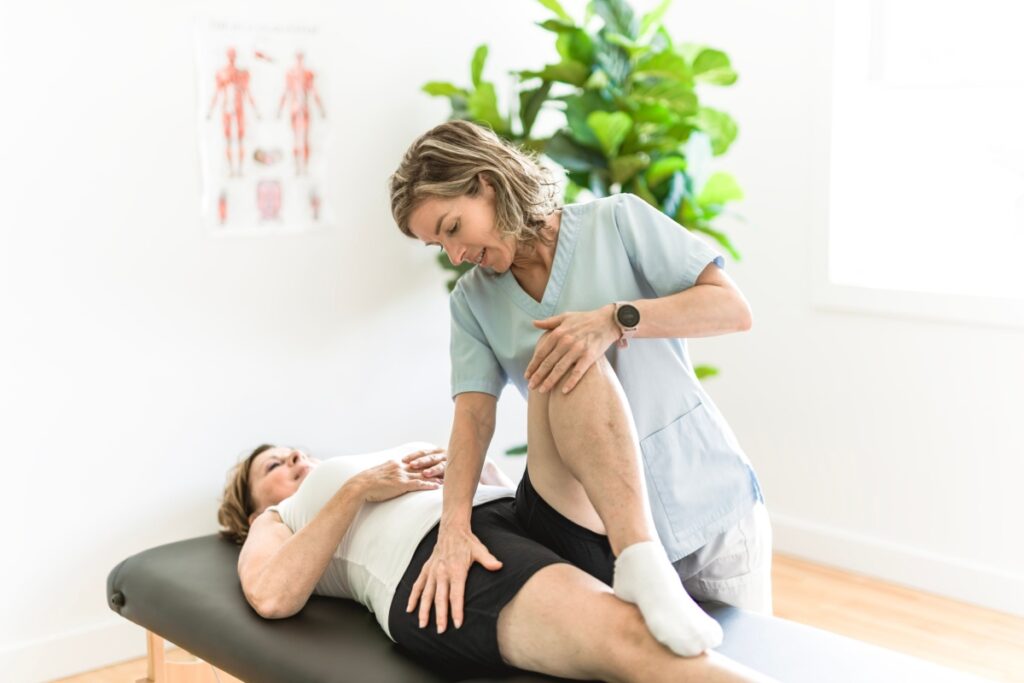 Physical therapist assisting a woman with a leg stretch during a physiotherapy session on a treatment table.